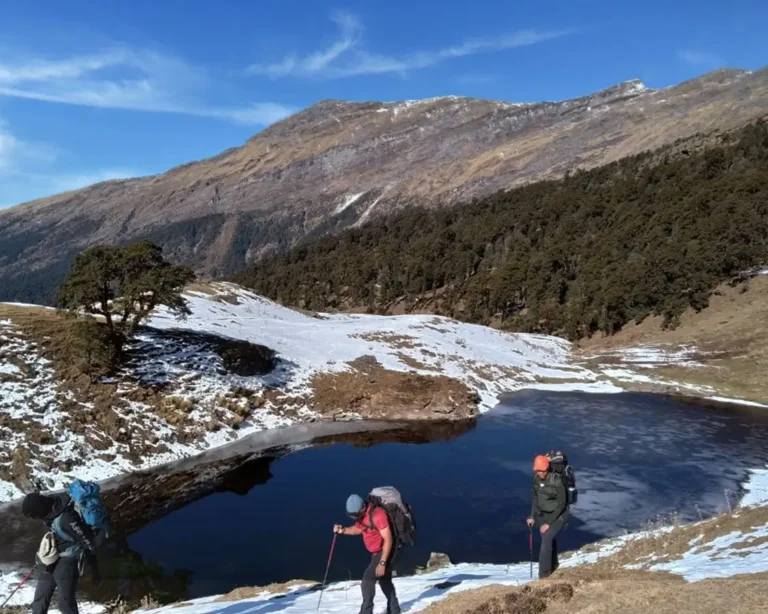 Trekkers walking past an alpine lake with snow patches